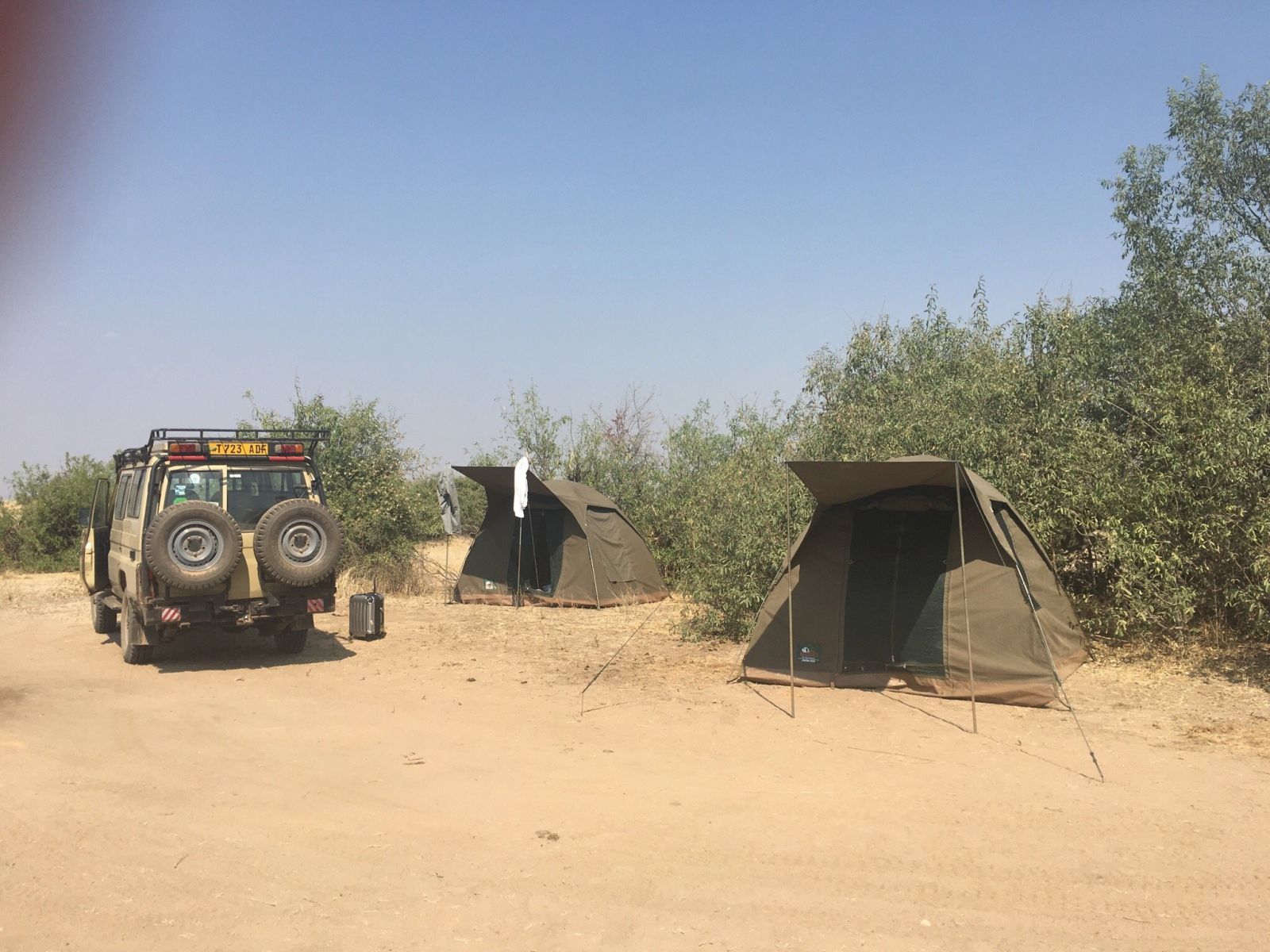 A safari Land Cruiser and two dome tents pitched at a sandy fly camp in Ruaha National Park