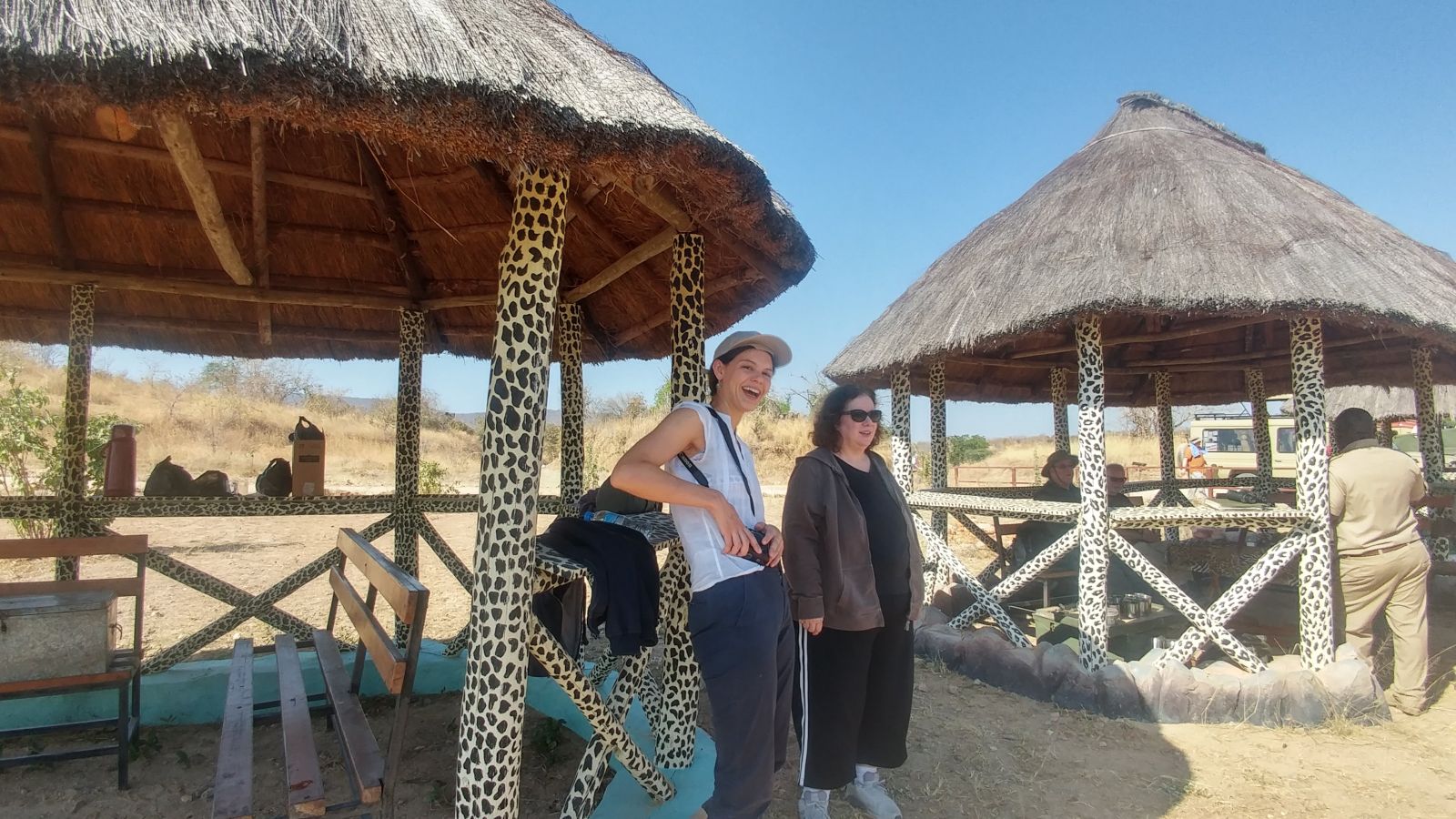 Two visitors standing beside thatched picnic shelters painted with a leopard-print pattern