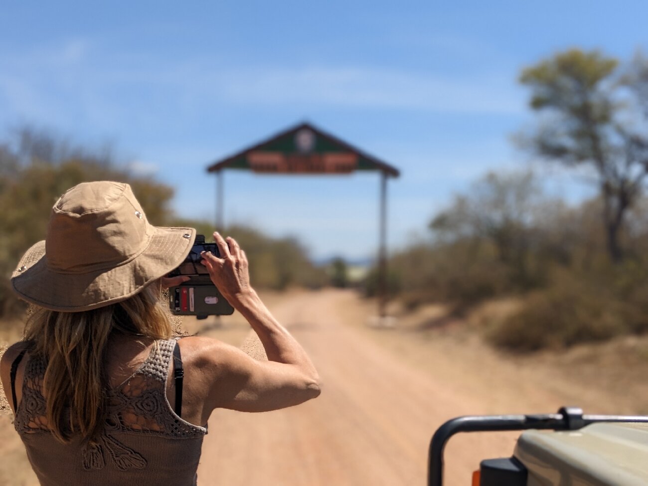 A visitor leaning from a safari vehicle to photograph the Ruaha National Park entrance gate